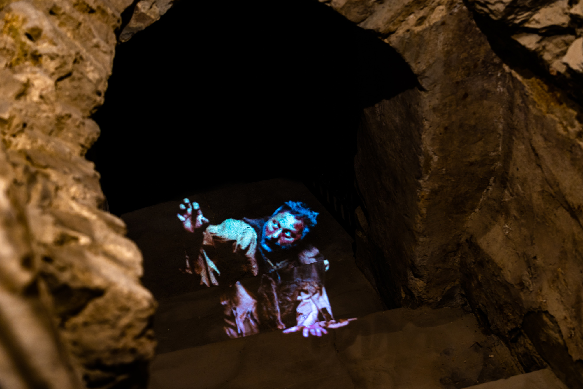 Nieoświetlony korytarz podziemi, z którego wyłania się hologram postaci mężczyzny wyciągającego rękę
